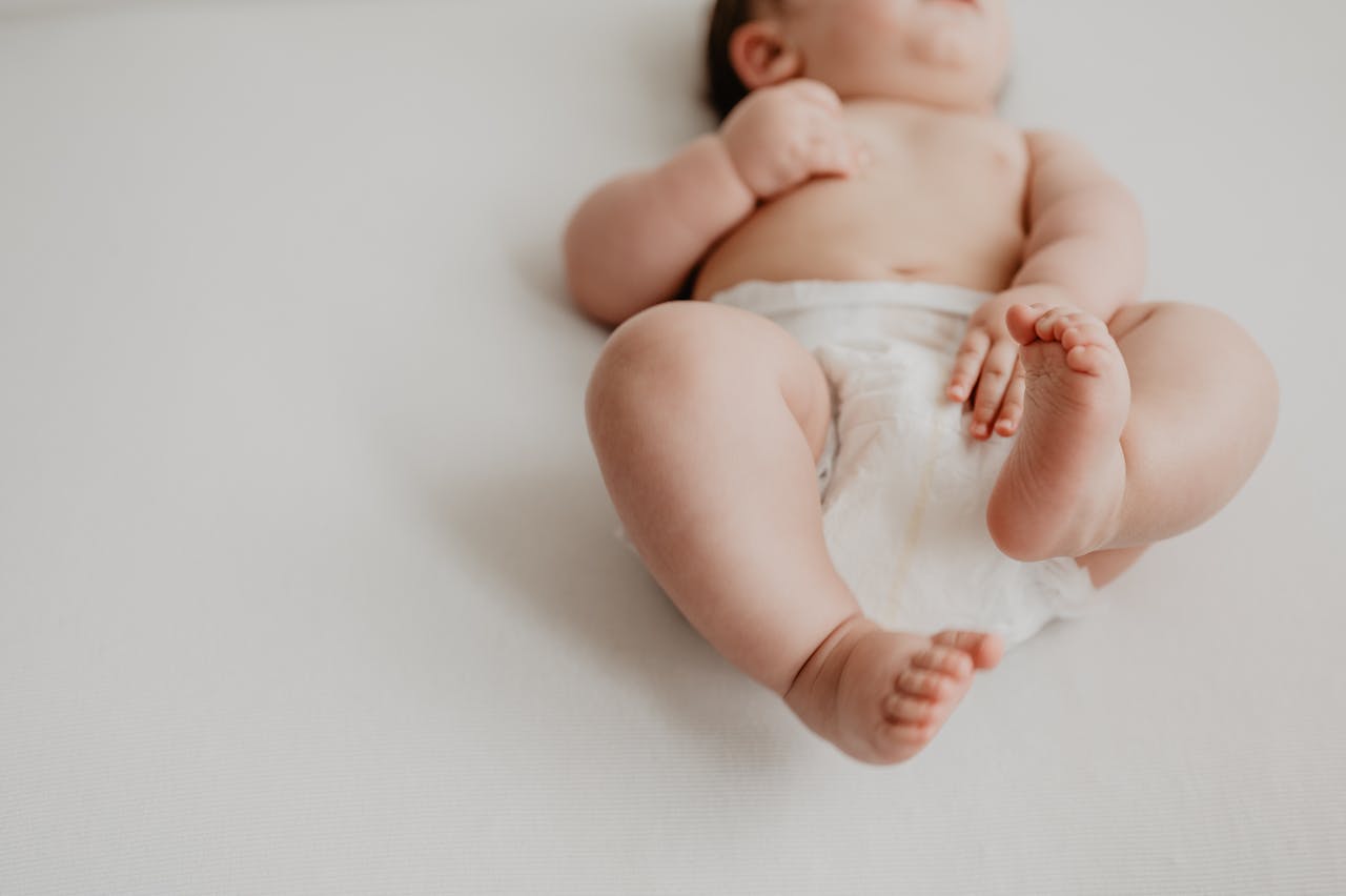 Cute baby lying on a white surface in a diaper, showcasing tiny feet and hands.
